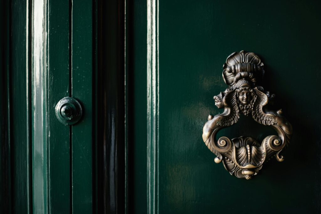 Close-up of a vintage brass knocker on a classic dark green wooden door, evoking a timeless elegance.